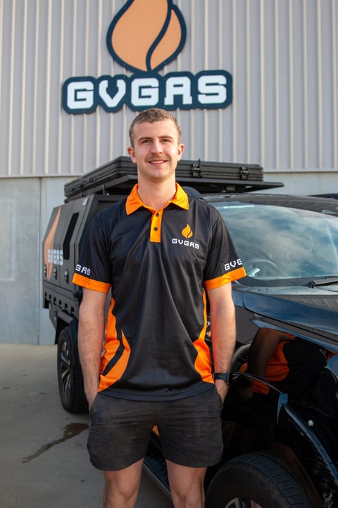 Male employee in GVAS branded polo shirt standing in front of company vehicle and building sign