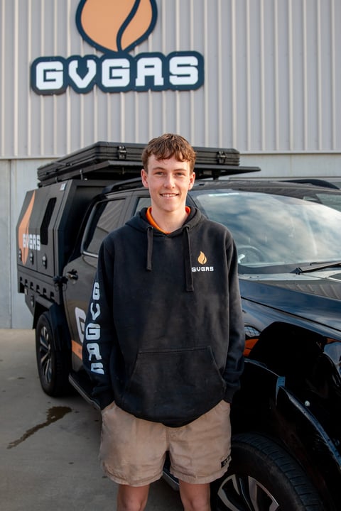 Young man in GVAS black hoodie standing in front of branded van and warehouse with GVAS logo