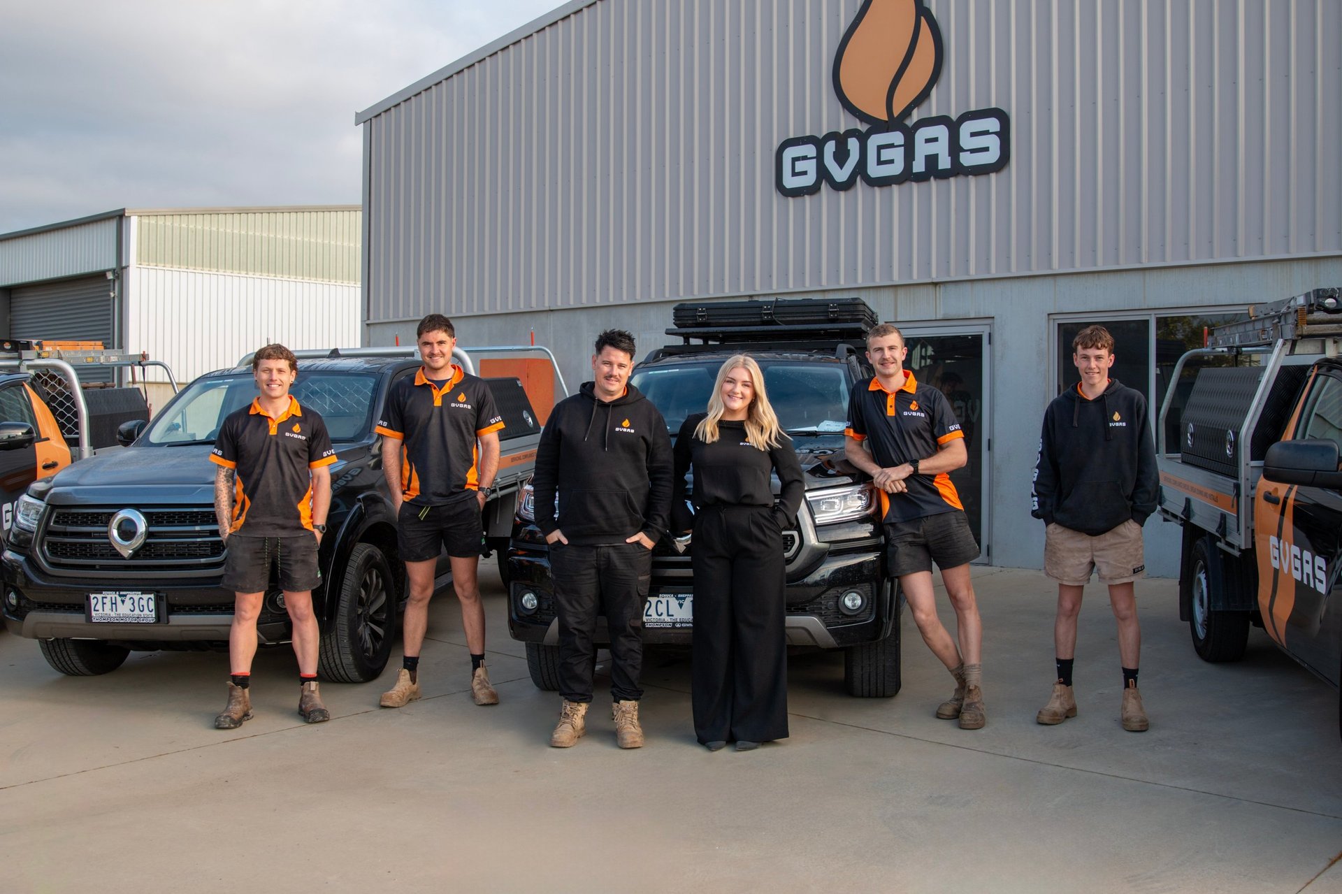 Team of workers in orange and black uniforms standing in front of black vehicles outside an Evoras industrial building